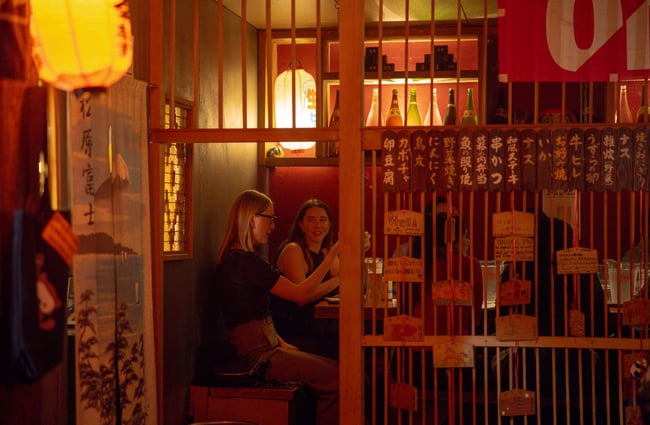 Two women sitting behind a screen at a table inside a darkly lit restaurant.