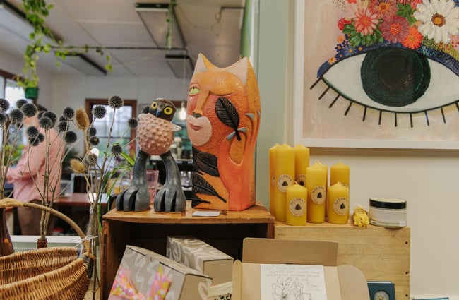 Bees wax candles and an abstract cat sculpture displayed on a shelf inside Tasteology.