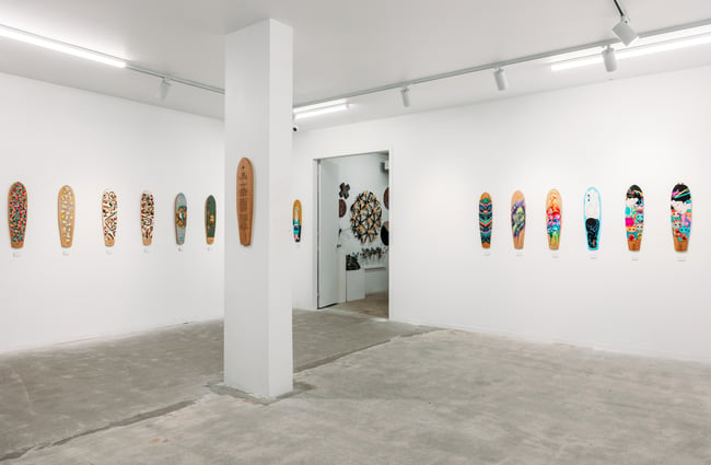 Works of art in the shape of skateboards on gallery walls.