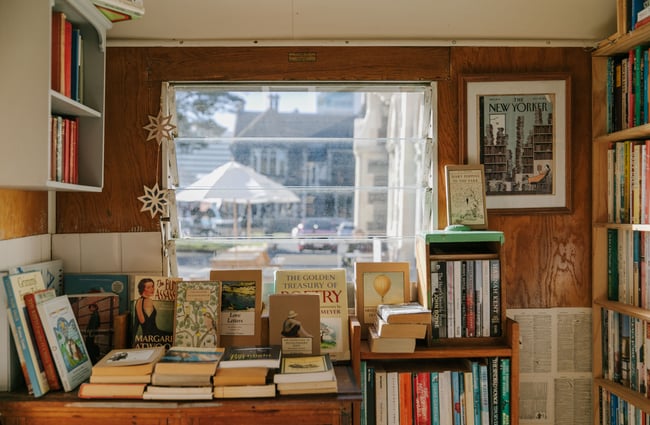 A close up of books on a bench and on shelves inside The Custard Square Bookshop.