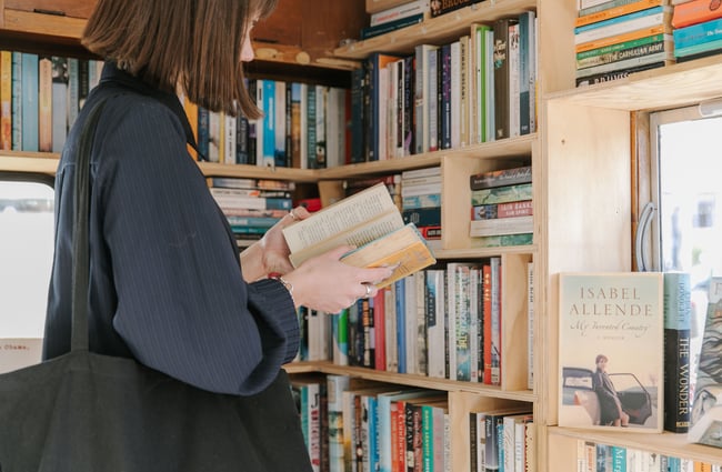 A woman standing inside the bookshop reading a book.