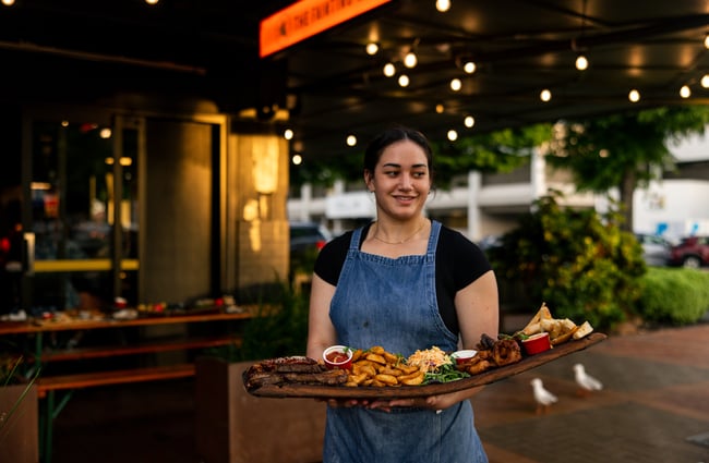 A female staff member holding a platter of food outside.