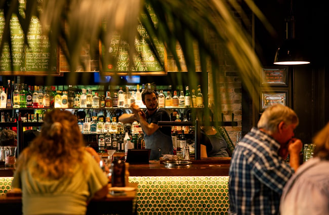 A bar man making a cocktail behind a bar.