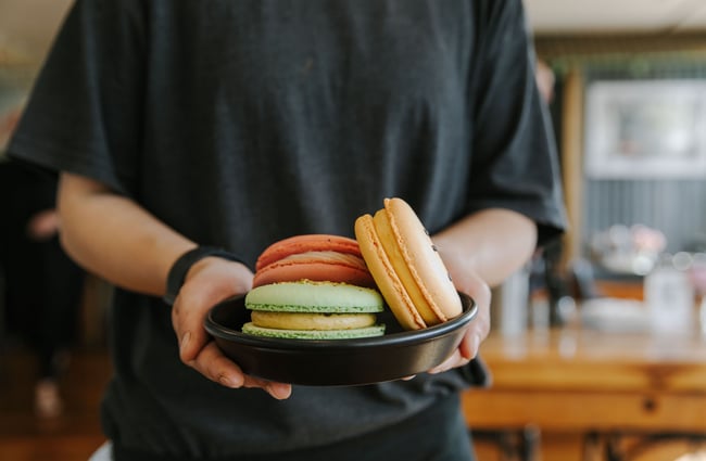 A staff member holding a plate of giant macarons at The Greedy Cow Café in Tekapo.
