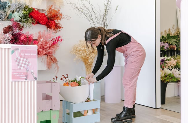 A lady in a black long sleeve and pink overalls bending over to look at a bouquet.
