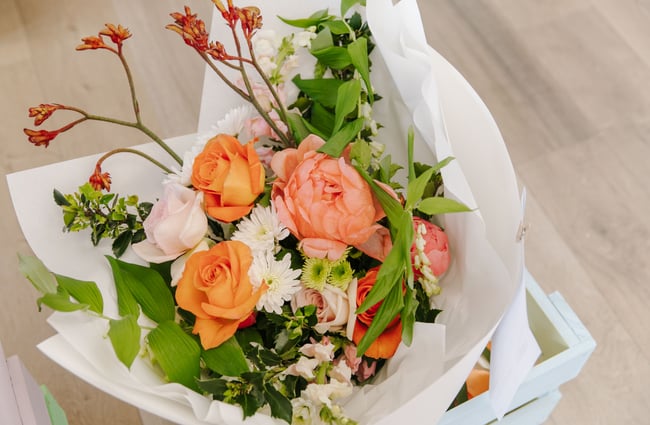 A close up image of an orange and white bouquet wrapped in white paper.