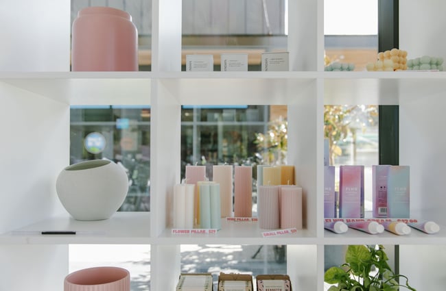 White cube shelving in the window of The Green Room store displaying candles and pots.