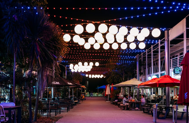 Large lights hanging over head outside a collection of bars at night