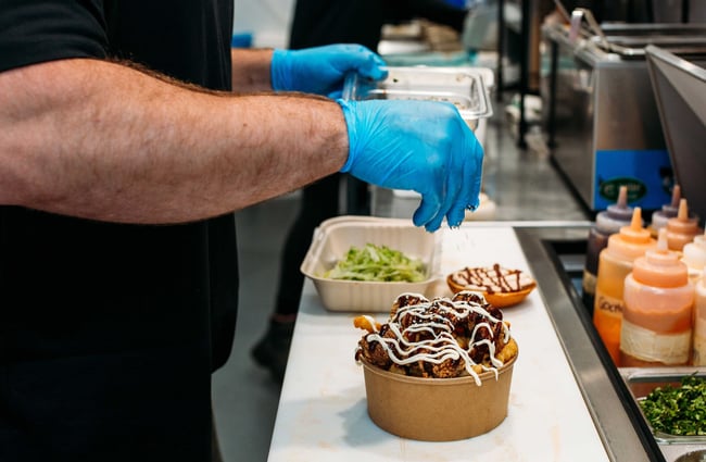 A chef wearing blue gloves preparing a container of fried chicken.