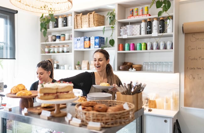 A woman smiling behind the counter at a cafe.