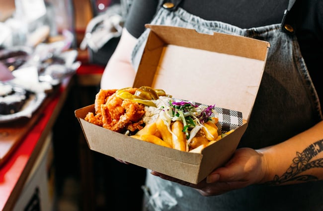 A worker at The Little Goat holding a cardboard container of loaded fries and chicken.
