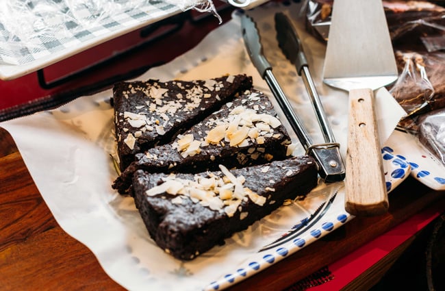 Three slices of a chocolate brownie with a pair of tongs next to it.