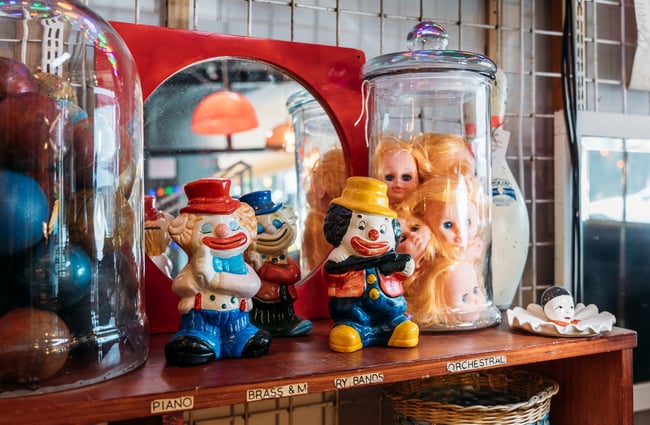 Close up of ceramic clown ornaments and a glass jar of doll heads at The Merry Go Round.