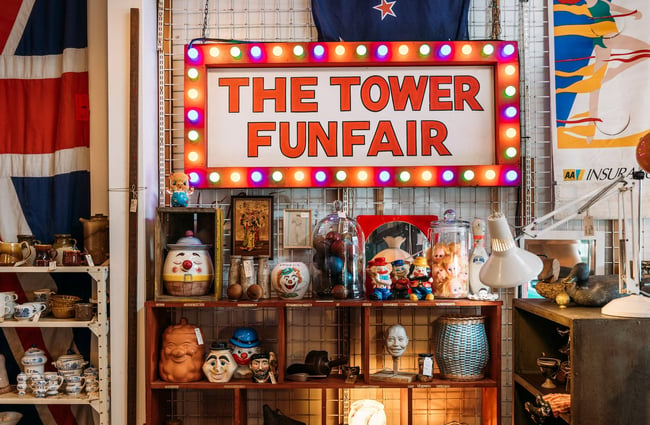 Clown ceramic jars and ornaments on shelves below a sign that says The Tower Funfair, bordered by colourful bulbs.