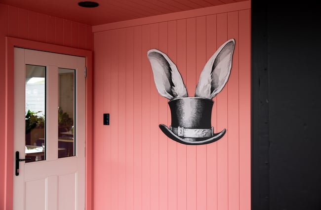 Rabbit ears coming out of a hat painted on a pink exterior wall.