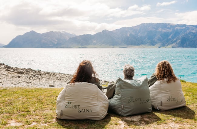 The backs of three people on bean bags looking out to a lake.