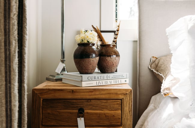 Two brown ceramic pots and two books on a wooden bedside table in The Workroom.