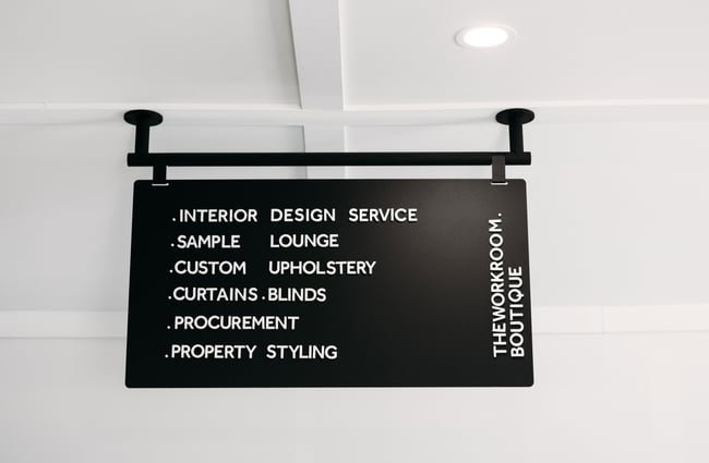 Black sign hanging from the ceiling with The Workroom's services displayed on it.