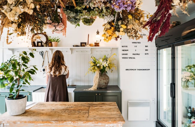 Dried flowers hang above a woman working behind the floristry counter in The Workroom