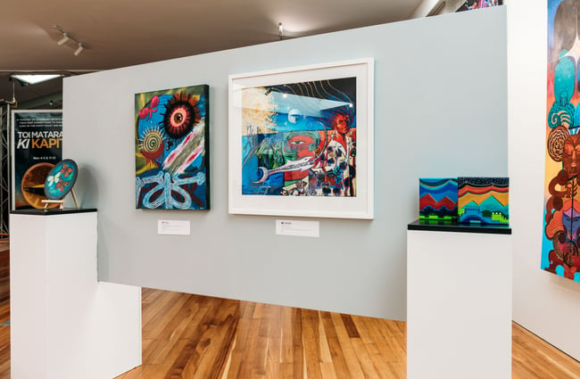 Colourful paintings on display on a white wall.
