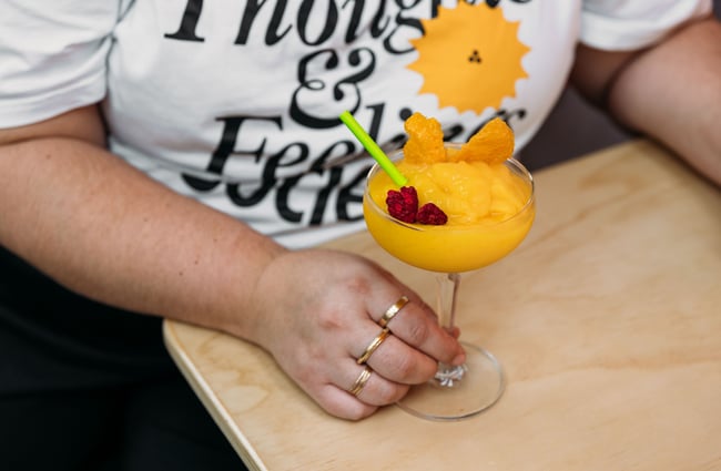 A hand holding an orange cocktail.