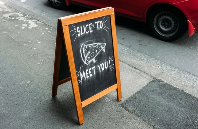 A small blackboard that says 'slice to meet you' on the sidewalk.