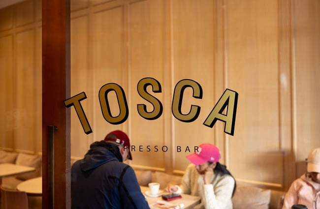 Golden 'Tosca' window decal with customers drinking coffee in background