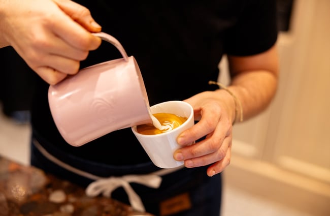 Barista pouring milk into coffee from a pink jug