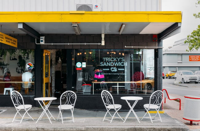 Exterior of Tricky's Sandwich Co with two white chairs and tables outside