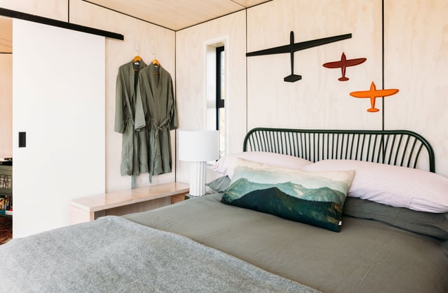 A bed inside a bedroom with art and dressing gowns hanging on walls.