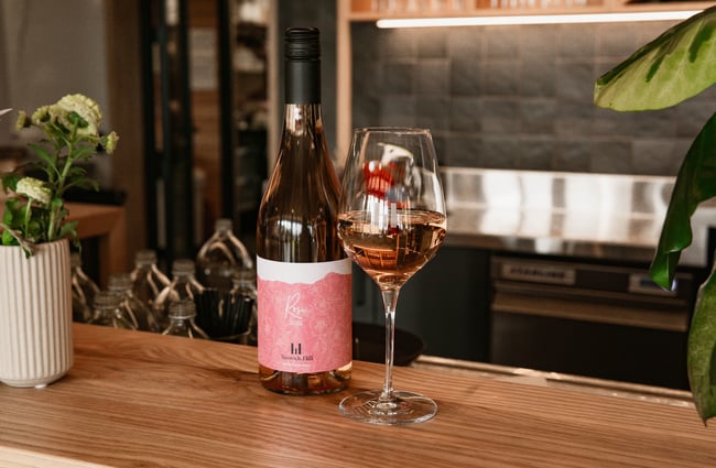 A bottle of Tussock Hill Rose 2022 and a glass of the rose sitting on the wooden bar inside the Tussock Hill restaurant.