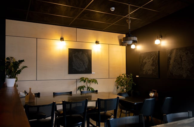 A cosy corner at Two Thumb Harbourside with green plants, dark wooden tables, abstract artwork and warm lighting