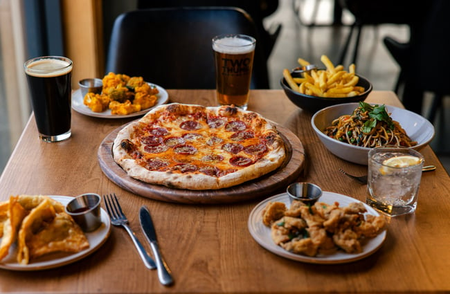 Table filled with pizza, fried food, chips, a bowl of soba noodles, beer and a gin and tonic