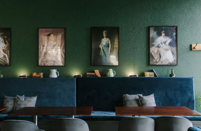 Plush blue seating set against a dark green wall filled with portraits of queens