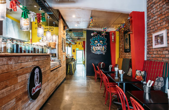 Colourful dining area inside Mexican restaurant with floral skull mural on wall