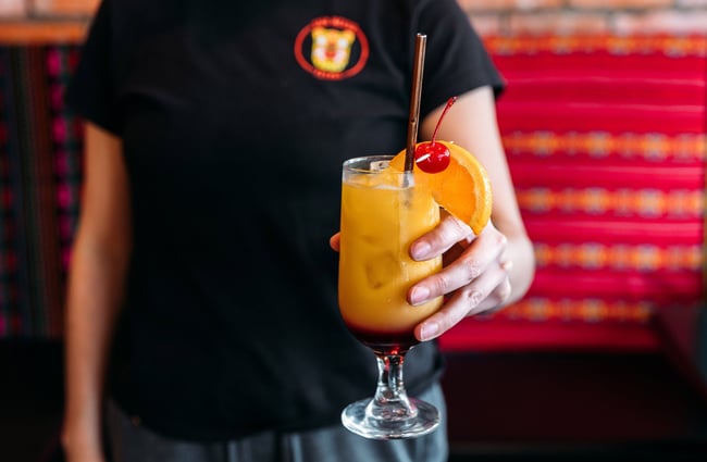 Someone holding a bright yellow Mexican-inspired cocktail with a cherry and slice of orange on the rim