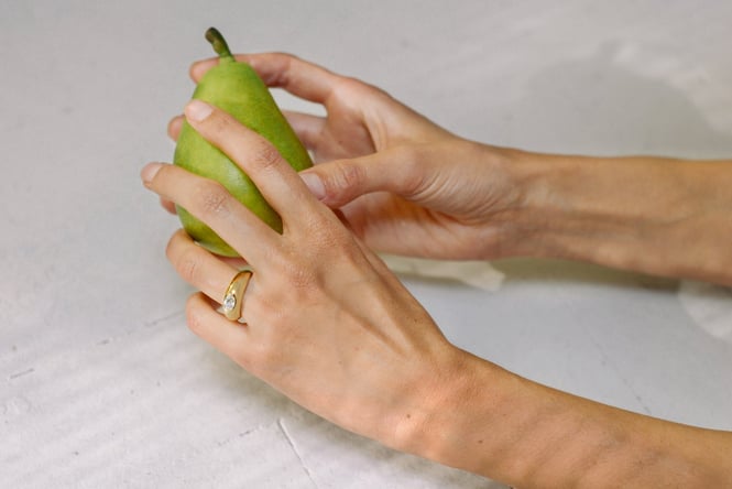 Two hands wearing rings holding a green pear.