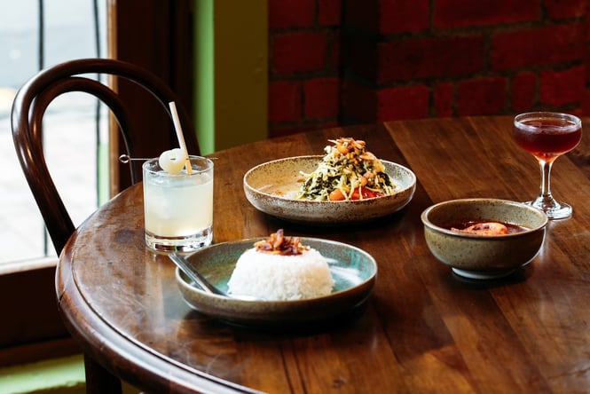 Two cocktails and three Burmese dishes on a table at Mabel's.