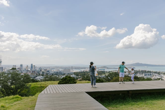 A family taking a photo at the top of Mt Eden with a beautiful view of Auckland in the background