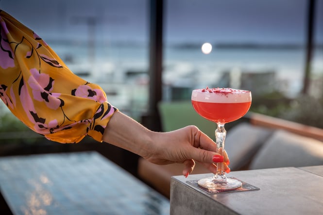 Someone holding a pink cocktail in a coupe glass