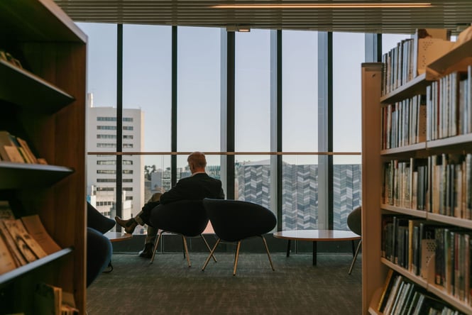 A man sitting in a chair looking out the massive windows at Turanga Christchurch library.