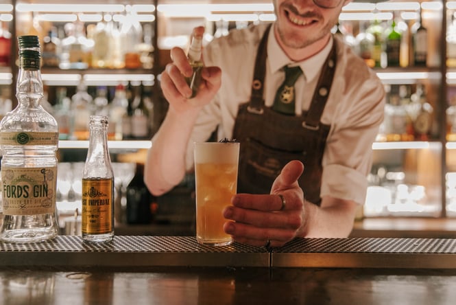 Bartender in suspenders mixing a cocktail in a long glass on top of the bar