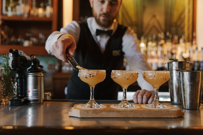 Bartender lining up three margaritas on a bar with chilli salt and dried citrus garnishes