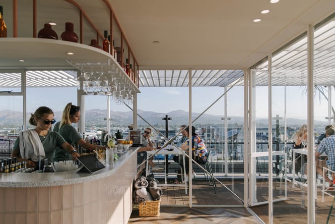 Two bartenders working at a rooftop bar with diners drinking on the balcony overlooking Christchurch New Zealand
