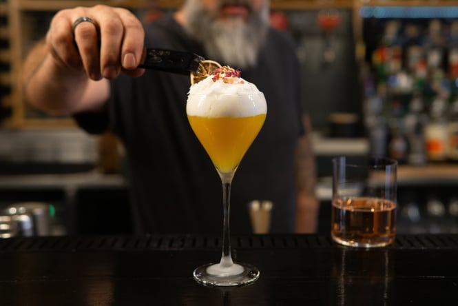 Bartender making a yellow sour cocktail with a dried citrus garnish on top