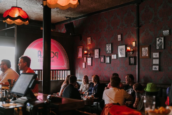 People enjoying a drink inside a dimly lit speakeasy bar with vintage wallpaper and decor