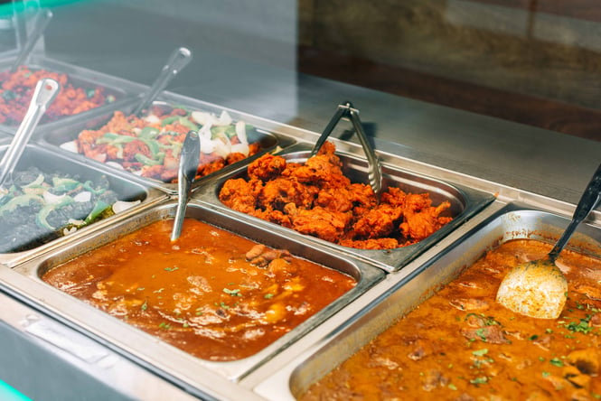 A close up of curry and other types of Indian food in a buffet counter.