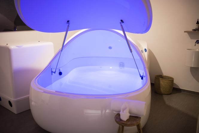 A blue lit float bath in a small white room.