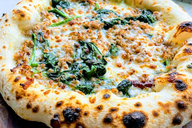 A close up of a cheese and spinach pizza on a table.