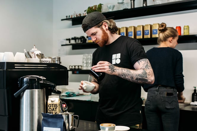 A tattooed man making coffee behind the counter at Workroom Havelock North.